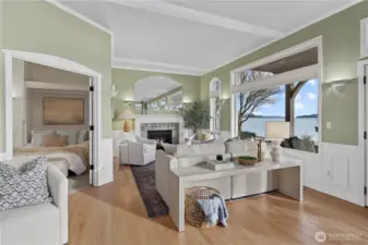 Bright and inviting living area with a cozy fireplace, large picture windows showcasing waterfront views, and an adjacent bedroom for flexible living.