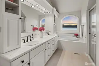 Spacious primary bathroom featuring dual vanities, soaking tub, separate shower, and a beautiful window framing serene waterfront views.