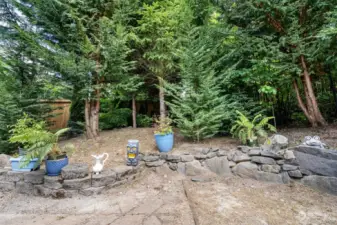 Mature Leyland Cypress trees provide greenery and privacy year around. Rock retaining wall to second tier of garden space.