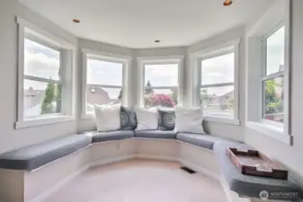 Reading nook framed by a stunning row of windows, this space offers panoramic views and abundant natural light.