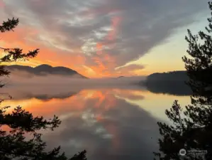 Warm golden hues reflect off the clouds and water as the sun rises over the mountain