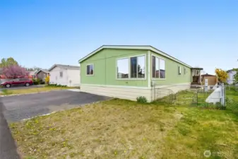Grassy front yard and gravel drive next to the paved parking. Three parking spaces.