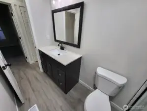 View of the vanity (and hallway) from the shower (dark room across is bedroom #2 we just saw). We are going to exit the bathroom and take a left, and immediately on our left will be bedroom #3.