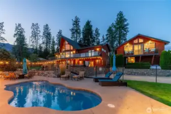 Twilight view of home with outdoor living area complete with pool, hot tub, dining and lounge areas, basketball court and detached carriage house.