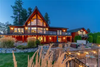 Twilight view of home w/ oversized windows, view decks, outdoor living area w/ pool, hot tub, basketball court, dining and lounge areas and detached carriage house.