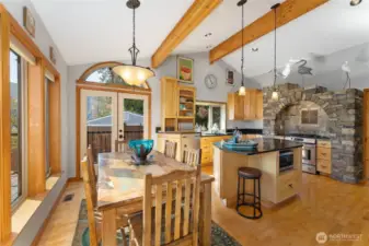 View of dining room and kitchen w/ hardwood floors, stainless steel appliances, quartz countertops, wood beams,  stone surround stove and oven, large windows with views of Lake Chelan and French doors leading to the outdoor living area w/ pool, hot tub, dining and lounge area.