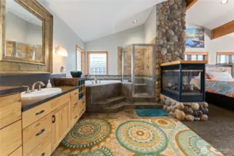 View of main level Primary Bedroom bathroom suite w/ stone fireplace, quartz countertops and soaking tub.