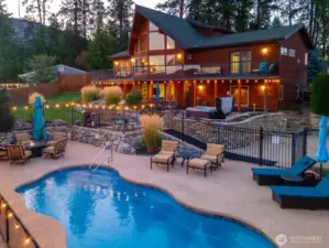 Twilight view of home w/ oversized windows, view decks, outdoor living area w/ pool, hot tub, lounge and dining areas, basketball court and landscaped grounds overlooking Lake Chelan.