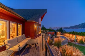 Twilight view of home w/ oversized windows, view decks, outdoor living area w/ pool, hot tub, basketball court, dining and lounge areas and landscaped grounds overlooking Lake Chelan.