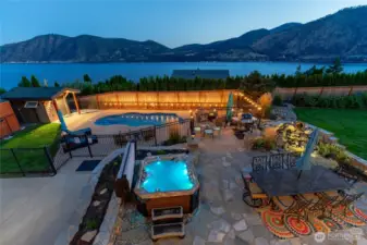 Twilight view of outdoor living area w/ pool, hot tub, basketball court, dining and lounge areas, landscaped grounds and water feature overlooking Lake Chelan.