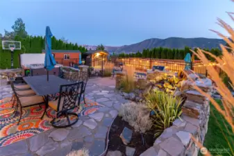 Twilight view of outdoor living area w/ pool, hot tub, basketball court, landscaped grounds, water feature and dining and lounge areas overlooking Lake Chelan.