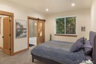 Inviting primary bedroom with serene forest views, cozy carpeting, and ensuite bath with sliding barn door.