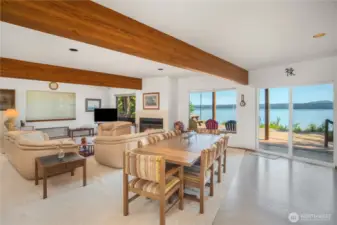 Open floor plan showcases breathtaking views of Hood Canal and the Olympic Mountains, with sliding doors that lead seamlessly to the spacious deck for indoor-outdoor living. The entry hall and stairs to the upper floor are behind you in this photo.