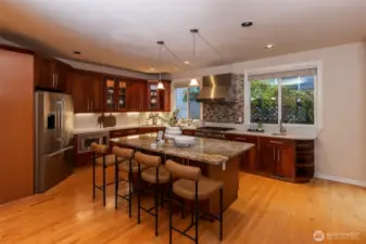 A beautifully remodeled chef’s kitchen featuring custom cherry cabinetry, premium Thermador and Bosch appliances, slab countertops, and a large centerpiece island perfect for gathering. Warm lighting and rich wood flooring create a refined, inviting atmosphere.
