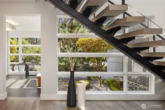 A signature moment—floating single-stringer staircase set against walls of glass, framing curated landscape and bringing natural light deep into the home.