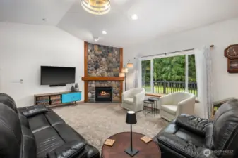 Main living room featuring vaulted ceilings, a stone fireplace, and large windows that bring natural light into the central gathering space.