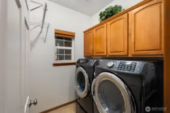 Dedicated laundry room with side-by-side washer and dryer, overhead cabinetry for storage, and a window for natural light.
