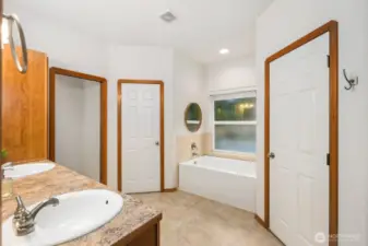 Spacious primary bathroom featuring a soaking tub beneath a window along with separate doorways leading to additional bathroom areas and storage.