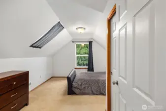 Upper-level bedroom with sloped ceilings and a window overlooking the surrounding trees, creating a cozy and private sleeping space.