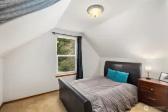 Additional view of the upstairs bedroom highlighting the angled ceiling lines and natural light from the window.