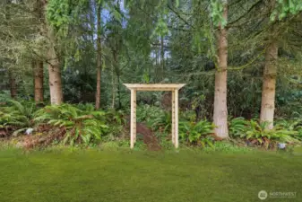 Wood garden arbor leading into a wooded area surrounded by mature evergreen trees and natural landscaping.