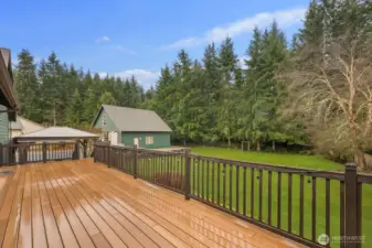 View from the deck overlooking the backyard lawn and detached outbuilding with surrounding trees.