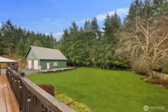 Raised deck perspective showcasing the open lawn, mature trees, and outbuilding beyond.