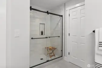 Primary bathroom shower with brand new floor to ceiling tile, fixtures and glass doors