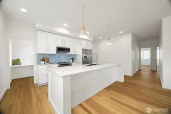 Looking across the island toward the kitchen with the walk-in butler's pantry to the left and the wide hallway to bedrooms and full bathrooms to the right.