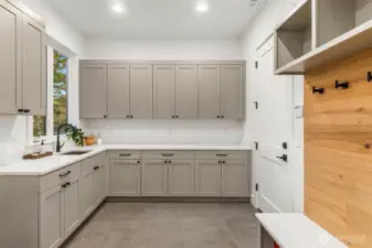Large Mudroom and utility room conveniently located off oversized 3 car garage and featured upper an lower cubbies, slab bench with coat hangers, TONS of storage in painted rift oak cabinets and stainless steel under mount sink with slab countertops