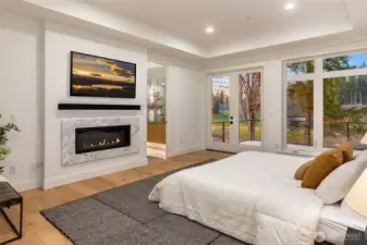 Stunning and dramatic expansive primary retreat features ceiling detail, contemporary fireplace with slab surround, wall to ceiling window wall with french doors leading to waterproof membrane deck