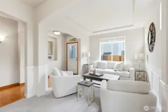 Formal living room with vaulted tray ceiling, wainscoting, and arched entry