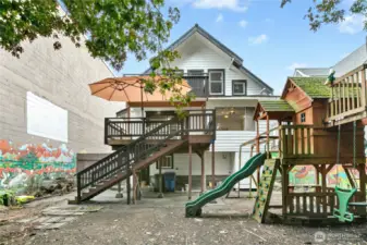 The fully-fenced backyard has a play structure, shady Japanese red oak trees, murals including a movie screen, and a large deck.