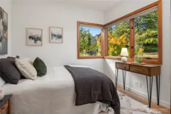 Main level bedroom with wide windows overlooking lush landscaping and fall color.