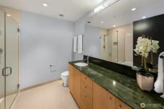 Spotless ensuite bath with large granite slab counters, glass shower and soaking tub.