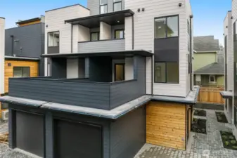 The back exterior shows off the layered design with wood accents, a balcony, and an attached garage.