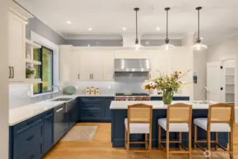 Blue Shaker cabinetry with sleek black door pulls, Quartz countertops, hand crafted Spanish tile backsplash, under cabinet lighting, Full wall ceramic tiled backsplash, Expansive kitchen island with undermount vegetable sink, room to seat 6, Stainless steel 48” six-burner Wolf range with stainless hood & dual ovens, 48” Sub-Zero Double Column refrigerator, Bosch dishwasher, GE Profile microwave built into island