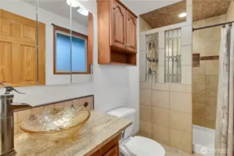 The primary bath has warm tile and a glass sink...
