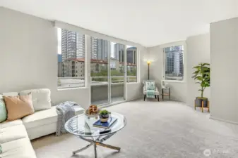 Cheerful living area with access to Juliet balcony and oversized windows for enjoying ample daylight and nighttime city lights.