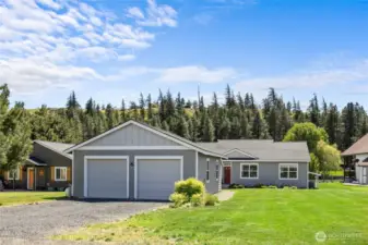 Charming home with gray siding, two-car garage, lush lawn, and a scenic forest backdrop. Great curb appeal!