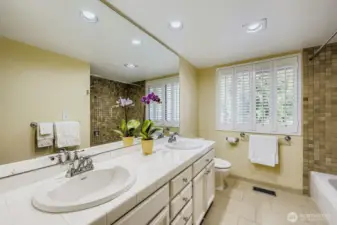 The guest bath also includes a large window with plantation shutter, dual sinks, abundant cabinetry and tile floors.
