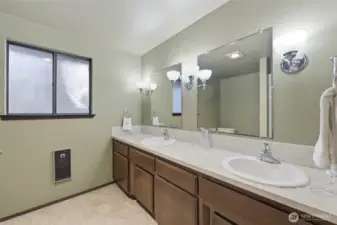 En suite primary bathroom features double sinks, privacy window for natural light, and ample space. Opposite the long vanity and double mirrors are the shower and commode.
