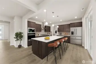 Large kitchen with stainless steel appliances, gourmet cooktop and hood-vent, quartz countertops, pendent lights, and breakfast bar. Photo of actual home with virtual staging.