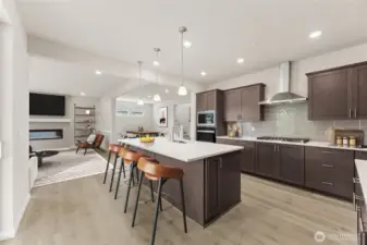 Large kitchen with stainless steel appliances, gourmet cooktop and hood-vent, quartz countertops, pendent lights, and breakfast bar. Photo of actual home with virtual staging.