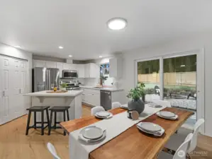 Open remodeled kitchen and dining area featuring white cabinetry, island seating, stainless steel appliances, and sliding door to access the fully fenced backyard