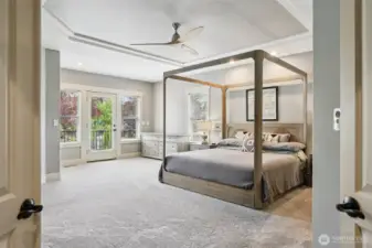 Expansive primary bedroom suite featuring plush carpeting, tray ceiling, ceiling fan, and abundant natural light. French doors provide direct access to the private deck, creating a seamless connection to outdoor living and enhancing the overall sense of space and comfort.
