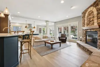 Open-concept main living area featuring hardwood floors, recessed lighting, and a floor-to-ceiling stone fireplace as a focal point. Large windows provide abundant natural light and views of the outdoor living spaces, while the layout flows seamlessly into the kitchen and dining areas—ideal for everyday living and entertaining.