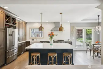 Open-concept kitchen centered around a large island with seating, quartz countertops, and custom cabinetry. The space flows seamlessly into the dining and living areas, enhanced by pendant lighting, wood flooring, and abundant natural light—ideal for everyday living and entertaining.