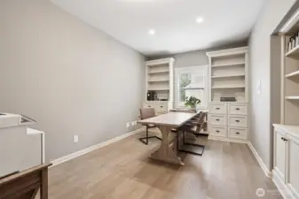 Lower-level office featuring custom built-in shelving and cabinetry, wood flooring, and recessed lighting. This quiet, well-designed workspace offers excellent flexibility for remote work, study, or creative use, with ample storage and a comfortable layout.