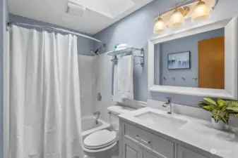 Recently updated hall bath with beadboard, tall vanity, curved shower bar, LVP flooring, and skylight.